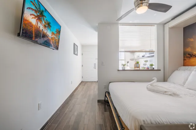 Bright and inviting bedroom featuring a modern ceiling fan, wall-mounted TV, and a serene decorative view, all enhancing a relaxing ambiance.