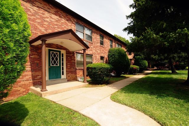 Charming brick apartment building with green door and well-maintained landscaping.