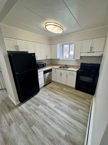 Modern kitchen with sleek black appliances, ample white cabinetry, and hardwood flooring.