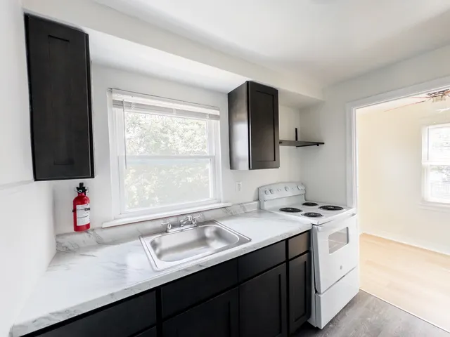 Bright and cozy kitchen featuring sleek black cabinets, marble-like countertops, and a modern stove, adjacent to a sunlit room with large windows.