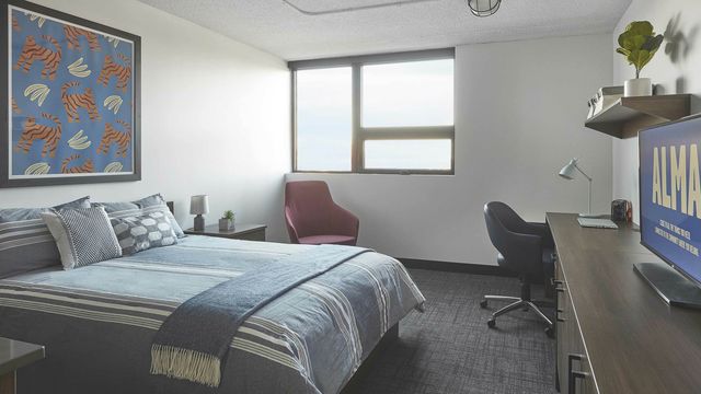 Inviting bedroom with large window, vibrant wall art, cozy bedding, and functional workspace.