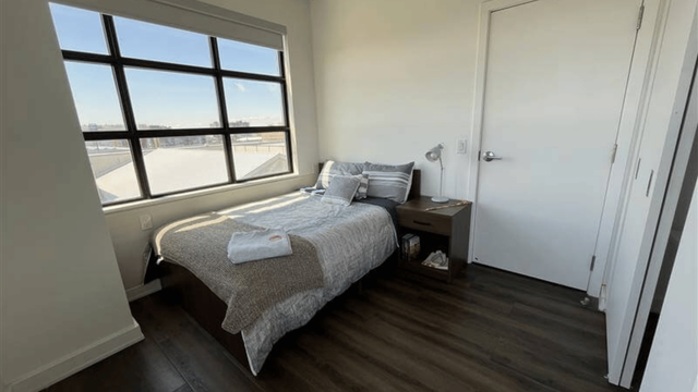 Cozy bedroom with large window offering skyline views and abundant natural light, complemented by chic decor and modern finishes.