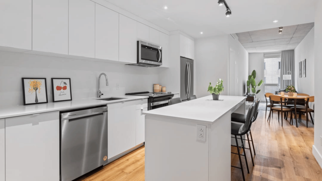 Modern open-plan kitchen with sleek white cabinetry, stainless steel appliances, and a stylish dining area with wooden flooring.