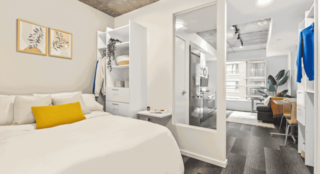 Bright and modern bedroom with cozy bed, stylish decor, and open view towards a chic living area with large windows and elegant furniture.