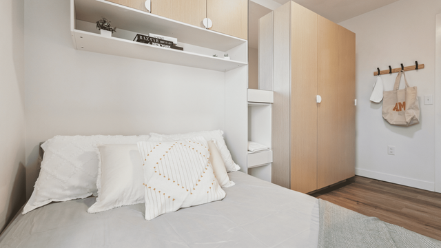 Modern bedroom with cozy white bedding, wooden cabinets, and chic wall shelving, offering ample storage and a serene atmosphere.