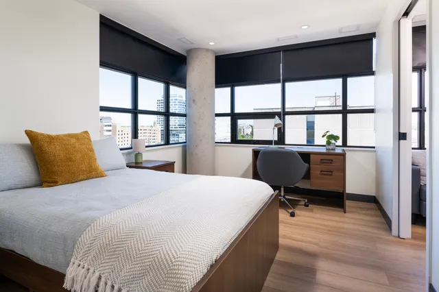 Bright, modern bedroom with city views, featuring sleek furniture and a cozy work space.