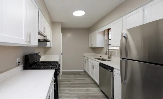 Modern kitchen with sleek white cabinets, stainless steel appliances, and elegant wood flooring, offering a stylish and functional space.