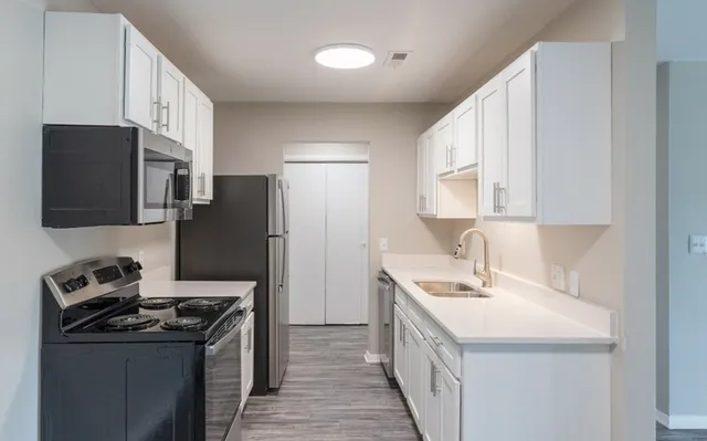 Modern galley kitchen with sleek white cabinetry, stainless steel appliances, and elegant countertop lighting.