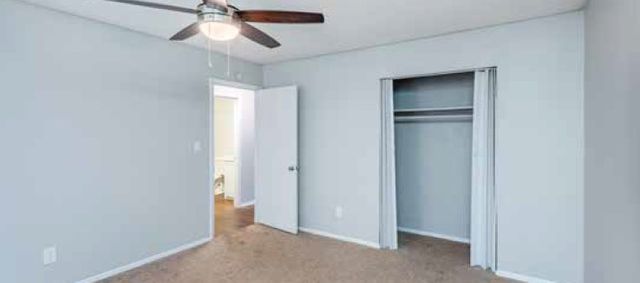 Bright and inviting bedroom with ceiling fan, open closet, and plush carpeting for a cozy ambiance.