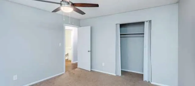 Bright and spacious bedroom with neutral tones, featuring a ceiling fan and ample closet space.