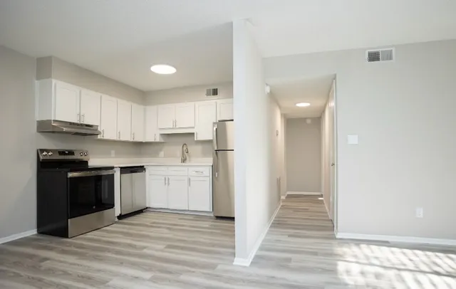 Modern kitchen with sleek stainless steel appliances, bright white cabinets, and elegant wood flooring.