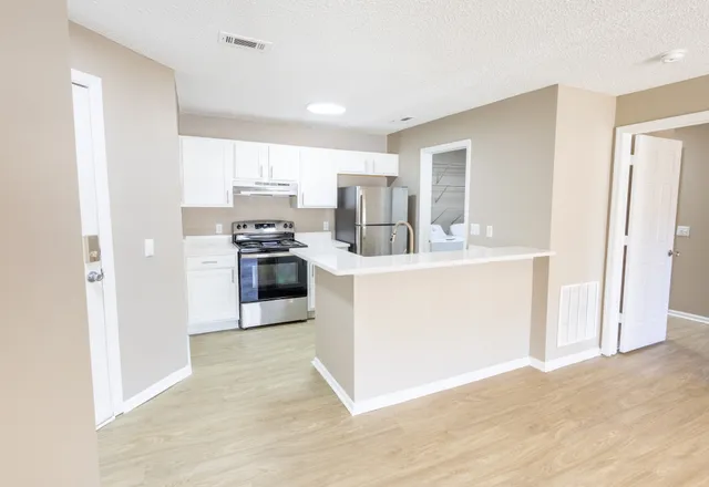 Modern apartment kitchen with sleek stainless steel appliances, white cabinetry, and a spacious countertop, complemented by light wood flooring.