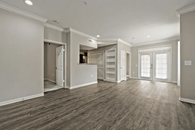 Bright and spacious open-concept living area with elegant wood flooring, stylish built-in shelving, and inviting French doors leading to a sunny patio.