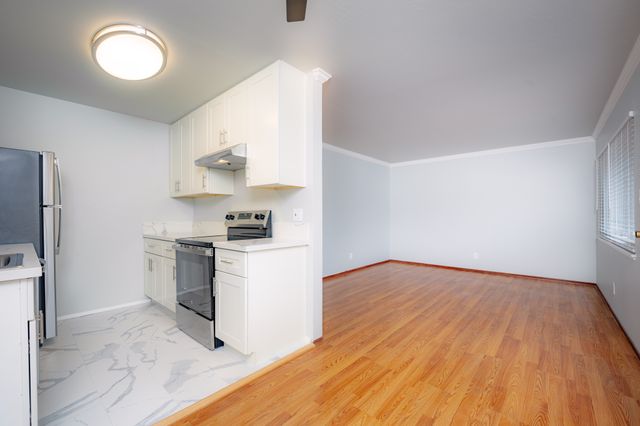 Modern open-concept living and kitchen area with sleek white cabinetry, marble tile flooring, and gleaming hardwood floors.