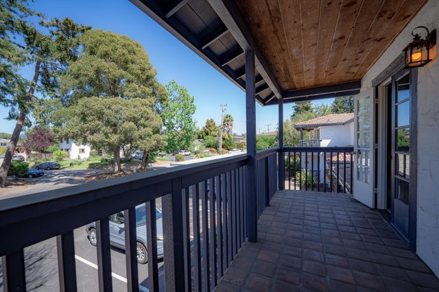 Charming balcony with a rustic wooden ceiling, offering a scenic view of lush green trees and a quiet neighborhood street.