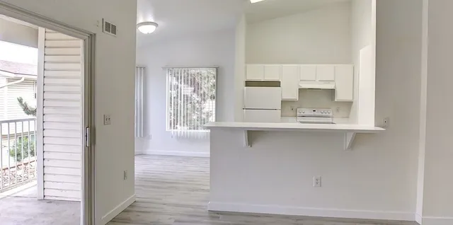 Bright open-concept kitchen with sleek white cabinetry, adjacent to a sunlit living area and balcony access.