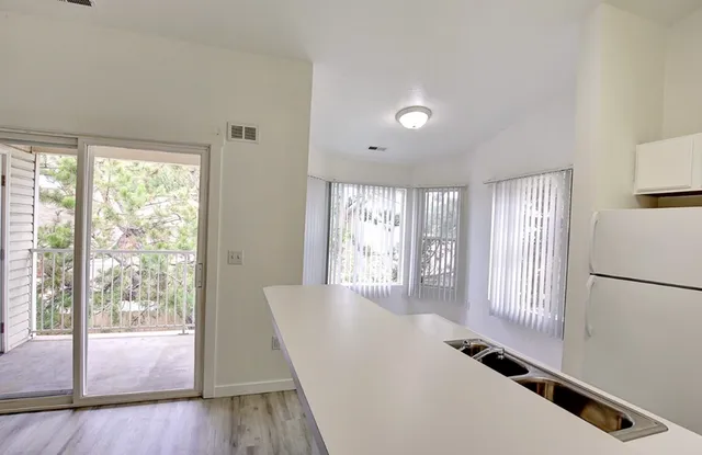 Bright and airy kitchen with an island, large windows, and a view of a private balcony surrounded by greenery.