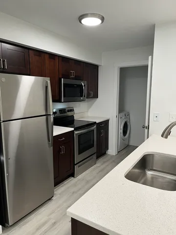 Modern kitchen featuring stainless steel appliances, sleek cabinetry, and an adjacent laundry area with contemporary flooring.