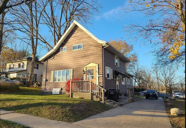 Charming two-story house with a front porch and spacious driveway, surrounded by a peaceful suburban landscape on a sunny day.