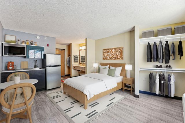 Chic studio apartment with modern kitchenette, cozy bed area, and open closet space featuring stylish decor and ample natural light.