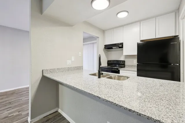 Modern kitchen with sleek granite countertops, double sink, black appliances, and white cabinetry.