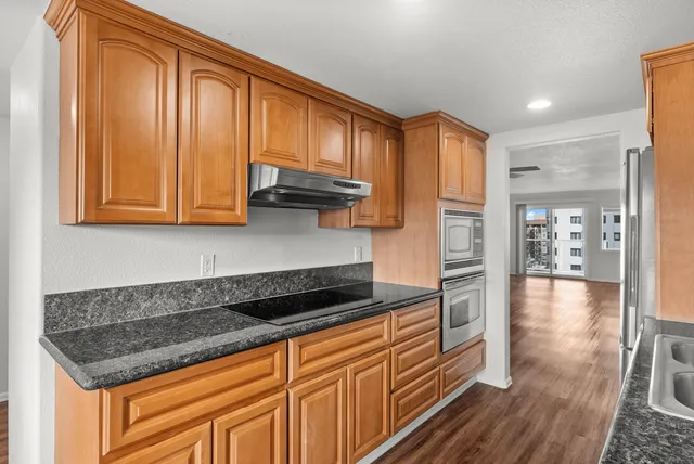 Modern kitchen with sleek wooden cabinets, granite countertops, and a view into a spacious living room.