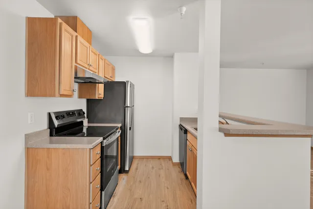 Modern kitchen with stainless steel appliances, light wooden cabinets, and laminate flooring, perfect for culinary enthusiasts.