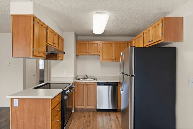 Modern kitchen featuring stainless steel appliances, wood cabinetry, and wood-style flooring in a well-lit apartment.