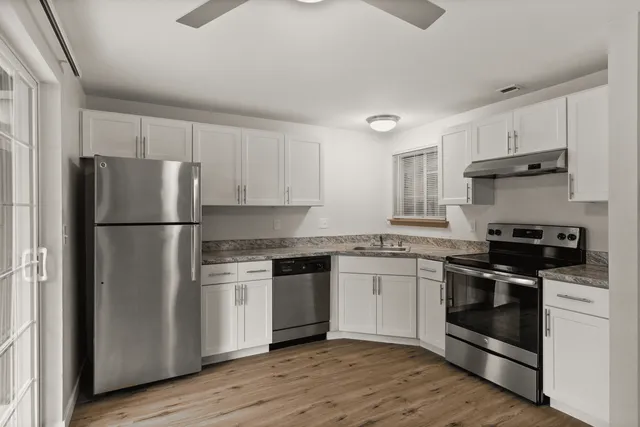 Contemporary kitchen with stainless steel appliances, white cabinets, and wood flooring.