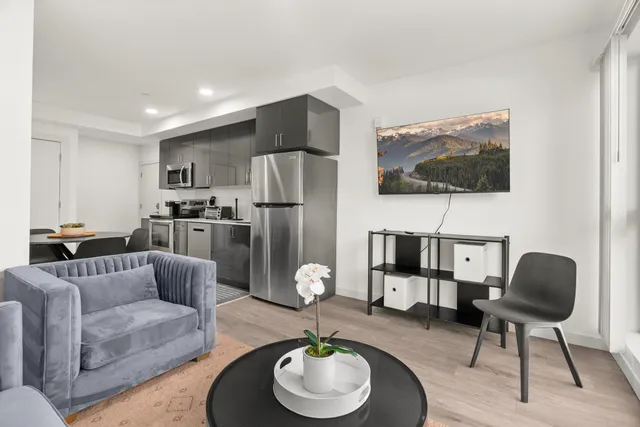Modern open-concept living area with sleek kitchen, stylish velvet armchair, and wall-mounted TV showcasing beautiful landscape view.