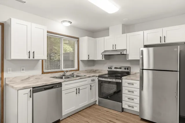 Modern kitchen with sleek stainless steel appliances, elegant white cabinets, and natural light through a large window.