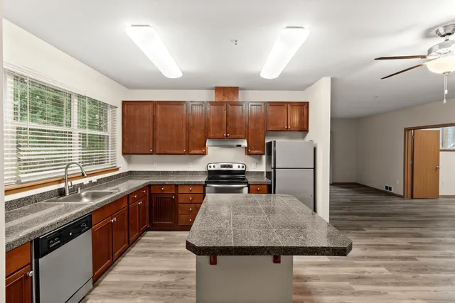Bright and modern kitchen with elegant dark countertops, stainless steel appliances, rich wooden cabinets, and open-concept design leading to a spacious living area.