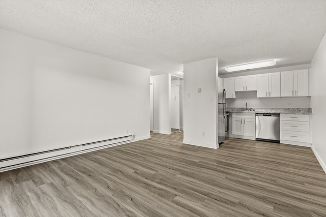 Open-concept living space with modern white cabinetry and stainless steel appliances on elegant wood flooring.