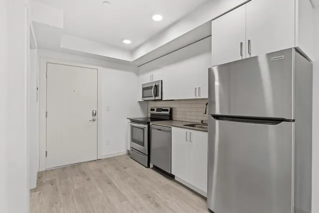 Modern apartment kitchen with stainless steel appliances, white cabinets, subway tile backsplash, and wood-style flooring