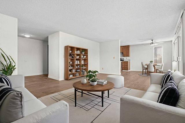 Elegant open-plan living area with modern white sofas, cozy dining nook, stylish wooden bookshelf, and lush indoor plants.