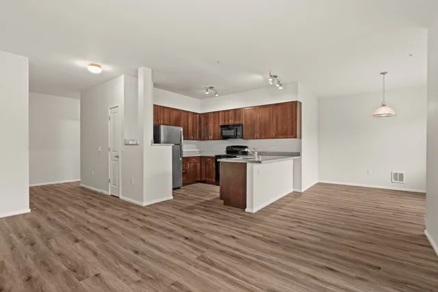 Modern open-concept kitchen with sleek wooden cabinetry, stainless steel appliances, and elegant pendant lighting over wood flooring.