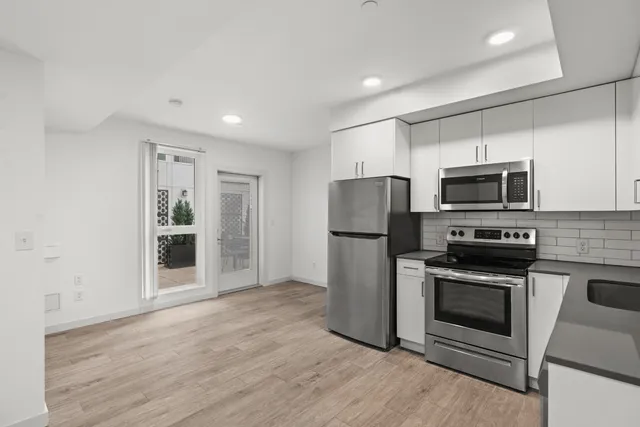 Modern kitchen with stainless steel appliances and sleek cabinetry, featuring beautiful wood-style flooring and direct access to a patio.