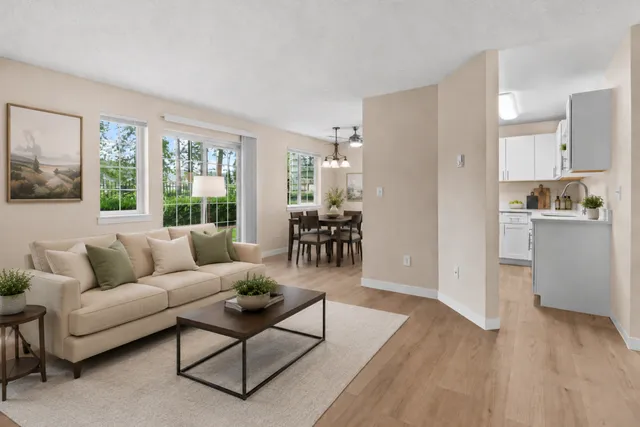 Inviting open-concept living and dining area with a cozy beige sofa, elegant wooden table, and modern kitchen in a bright, airy apartment.