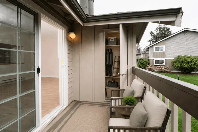 Charming apartment balcony with comfortable seating, lush greenery, and a sliding glass door leading to the cozy interior.