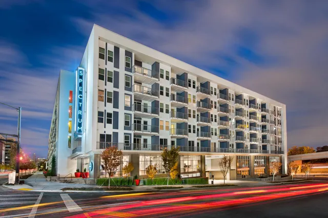 Modern apartment building with illuminated Spectrum sign, featuring multiple balconies and vibrant evening lighting.