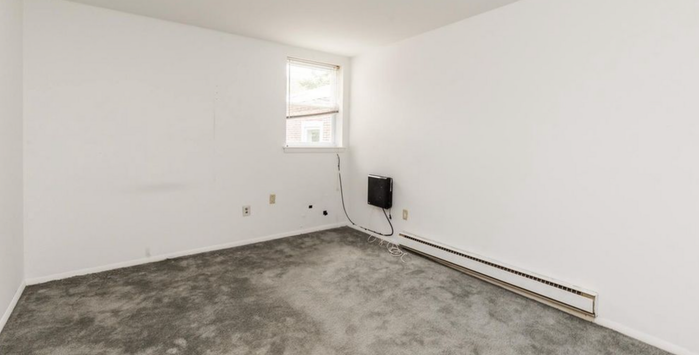 Bright, freshly painted empty room with plush gray carpet and a large window, ideal for customization and natural light.