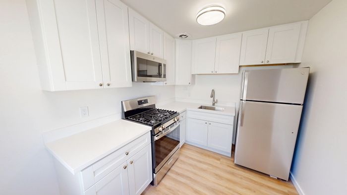 Modern kitchen with sleek stainless steel appliances, bright white cabinetry, and elegant wooden flooring.