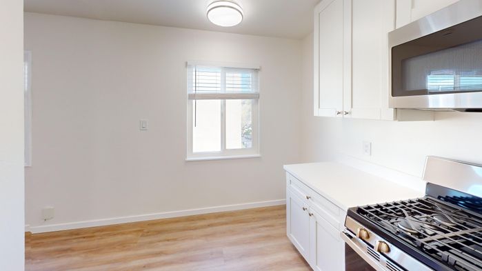 Bright and modern kitchen with sleek white cabinetry, stainless steel appliances, and warm wood flooring bathed in natural light from a sunny window.
