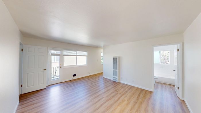 Bright and inviting living room with sleek hardwood floors, large window providing natural light, and an accessible door leading to the outdoors.