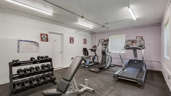 Bright, well-equipped fitness room featuring treadmills, weights, and motivational decor.