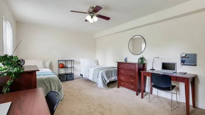 Inviting bedroom with two beds, wooden furniture, and a dedicated workspace featuring a laptop and desk lamp.