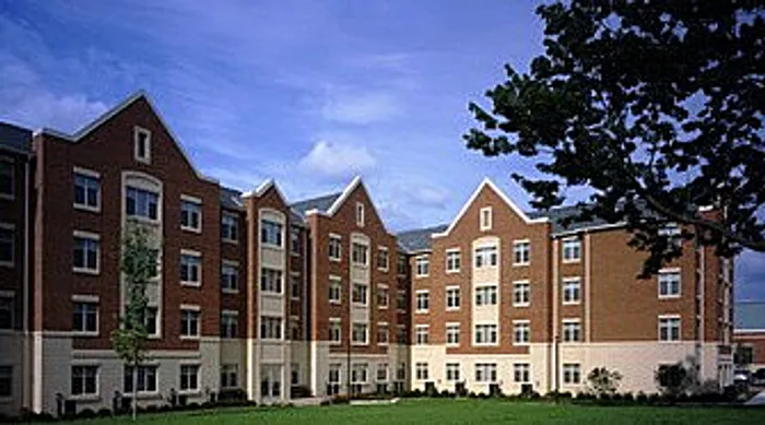 Inviting four-story brick apartment building with lush green landscaping and a clear blue sky.