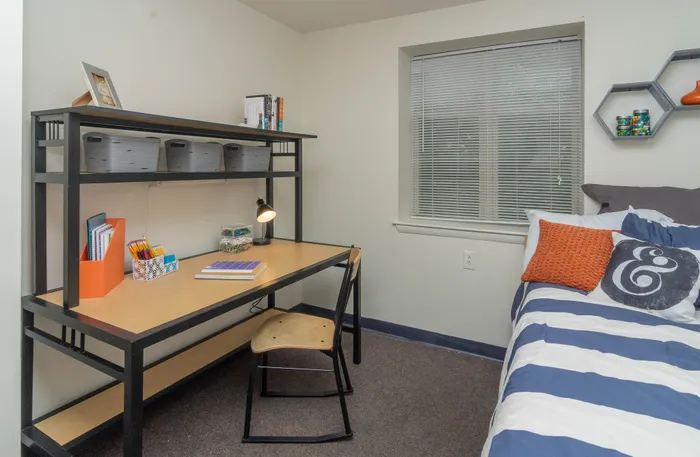 Bright room with a modern desk setup, comfy bed, and decorative shelving.