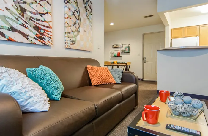 Inviting living room with modern artwork, a plush brown sofa, and vibrant pillows showcasing a blend of comfort and style.