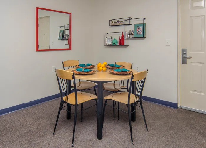 Inviting dining area with a table set for four, complemented by a vibrant red mirror and decorative shelves.